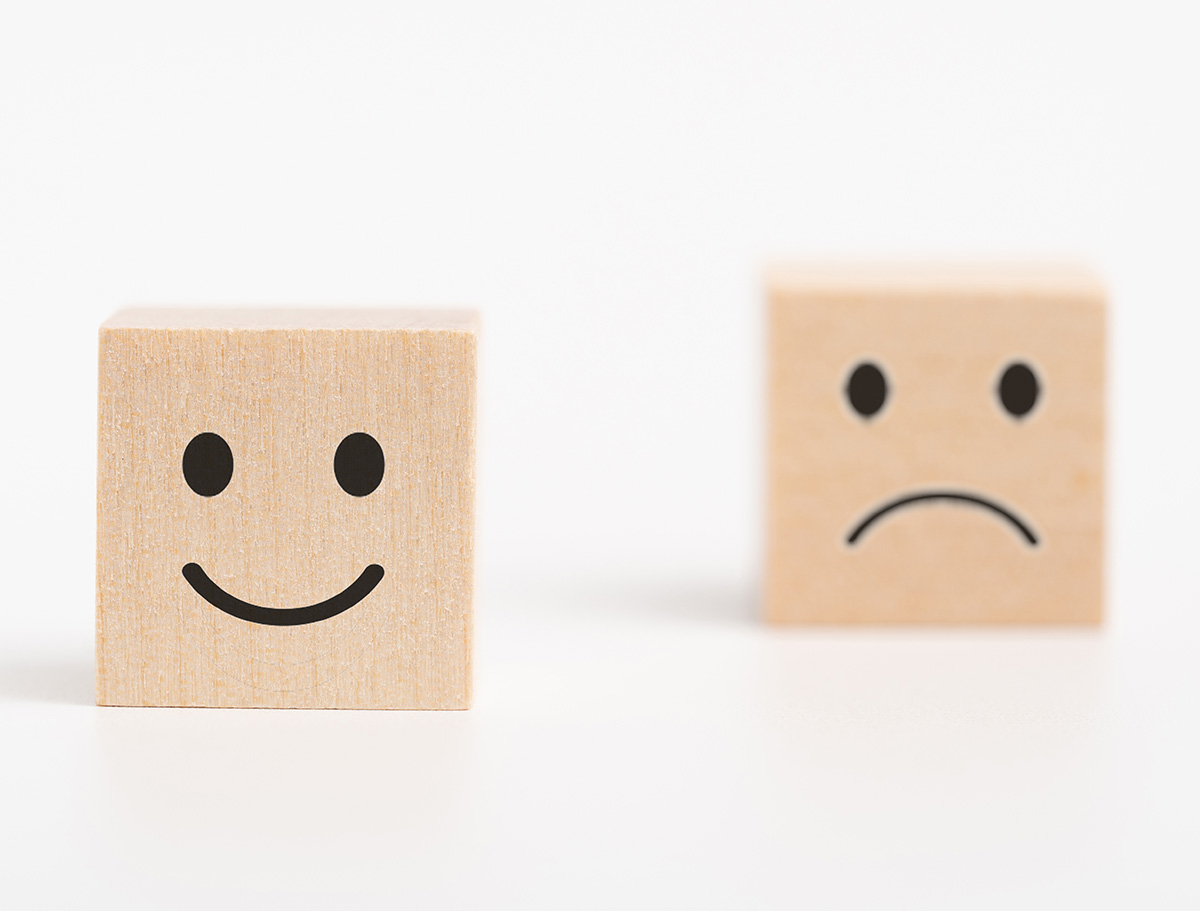 Ein Holzwürfel mit einem traurigen Smiley und einer mit einem happy smiley